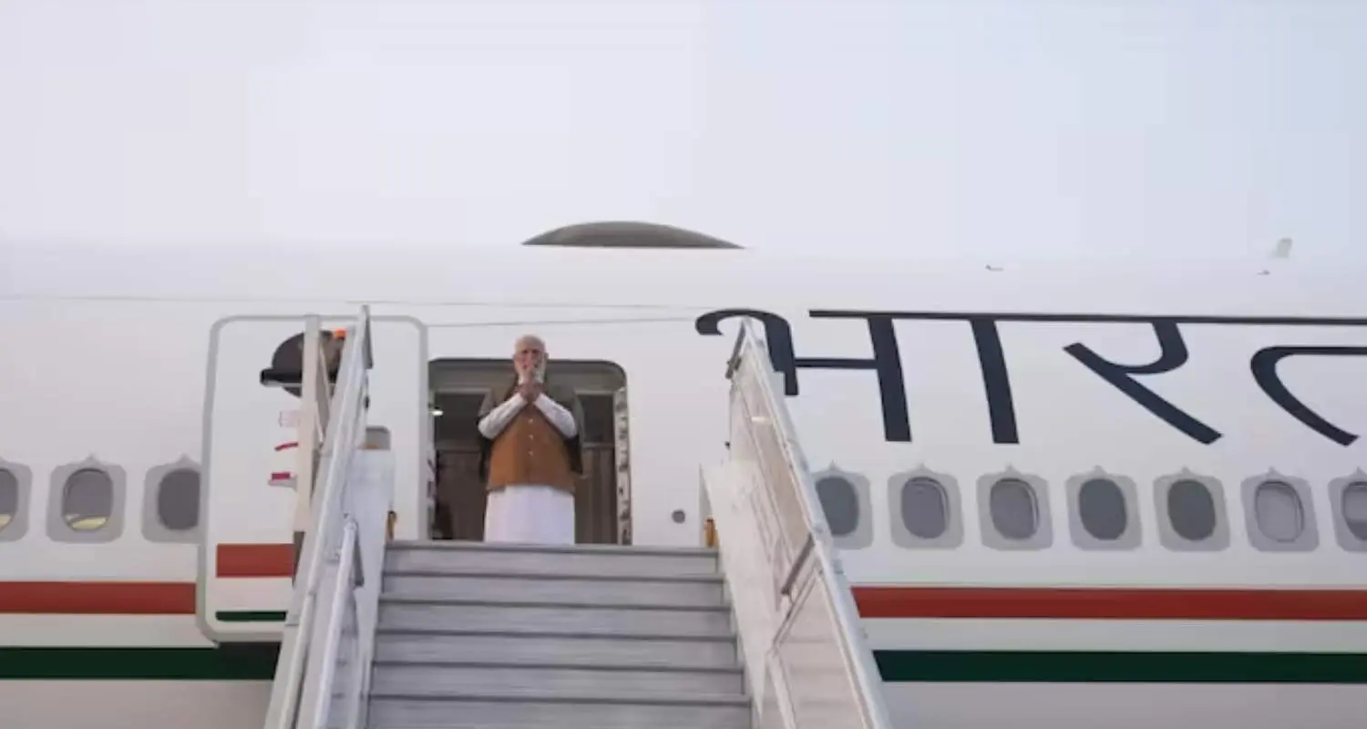 Prime Minister Narendra Modi stands at the top of the aircraft stairs with hands folded in a traditional greeting before departing on a 'Bharat' branded government plane. 