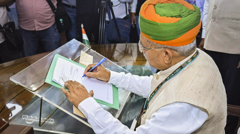 Arjun Ram Meghwal signing official documents while assuming charge as India's Law Minister, wearing a saffron and green turban and MP Lok Sabha lanyard.