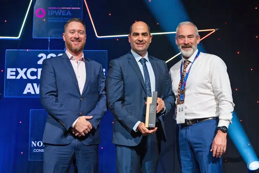 Three men standing on stage at the IPWEA Queensland Northern Territory 2023 Excellence Awards, with the center individual holding a trophy.