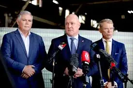 New Zealand Police Minister Mark Mitchell, Prime Minister Christopher Luxon, and Justice Minister Paul Goldsmith stand before microphones at a press conference.