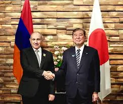 Japanese and Armenian officials shaking hands in front of national flags during the exchange of diplomatic notes ceremony in Yerevan.