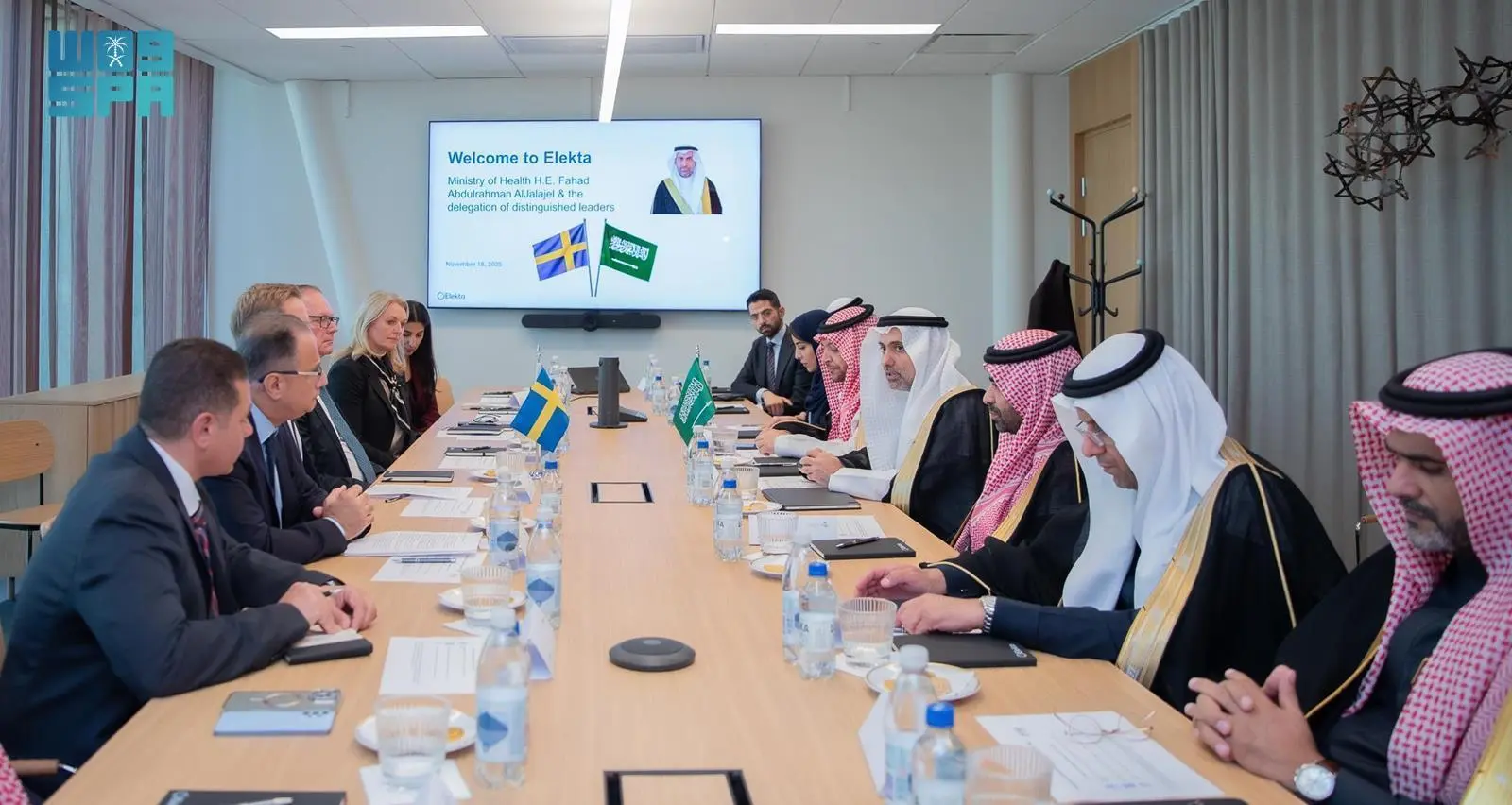 Saudi Minister of Health Fahad AlJalajel and his delegation seated at a conference table opposite Elekta executives during a meeting in Stockholm, with Swedish and Saudi flags displayed alongside a presentation screen welcoming the ministry.