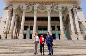 UK Minister for the Indo-Pacific Seema Malhotra (center) stands with officials on the steps of the Vidhana Soudha in Bengaluru, with the inscription 'Government Work is God's Work' visible above.