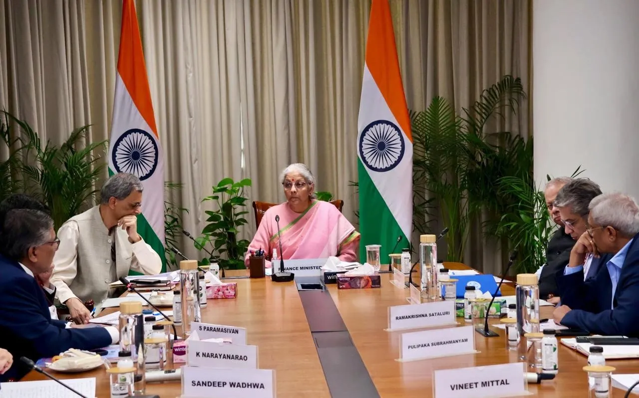Union Finance Minister Nirmala Sitharaman presiding over a meeting with officials and industry representatives at a conference table flanked by Indian flags.