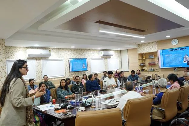 Advocate Ms. Janvi Satpal Babbar standing and addressing a conference room full of employees during a POSH Act orientation, with screens in the background displaying presentation slides titled 'QUID PRO QUO