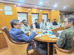 A group of government officials sitting around a large wooden conference table equipped with microphones and water bottles during a formal meeting at Haj House, Mumbai.
