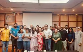 Group of organizers and delegates standing together for a photograph at a Kashi Tamil Sangamam event venue with a projection screen in the background.