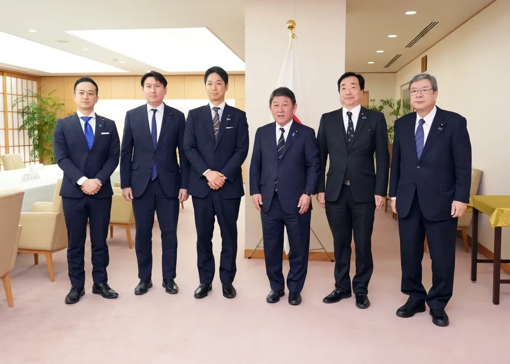 A group photo of six men in suits standing in a row indoors with a Japanese flag in the background. Japan's Foreign Minister Toshimitsu Motegi stands center-right, and Japan Innovation Party Co-Representative Fumitake Fujita stands center-left.