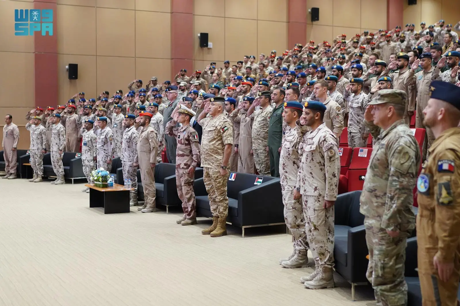 Military personnel from the Royal Saudi Air Force and allied nations stand and salute in an auditorium during the conclusion of the ATLC-35 exercise in the UAE.