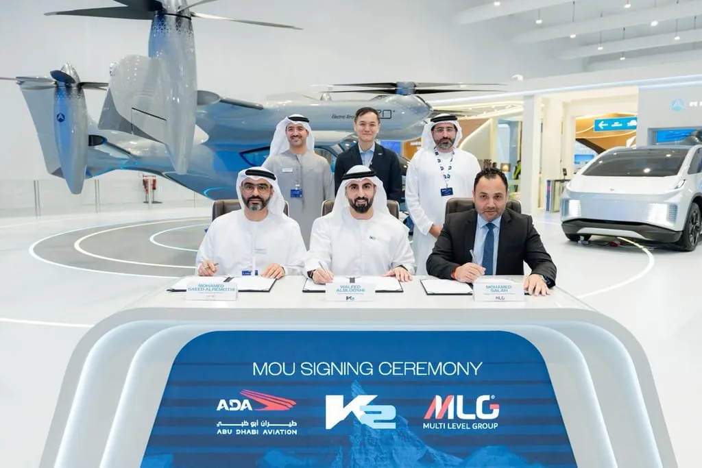 Executives from Abu Dhabi Aviation, K2, and Multi Level Group sit at a desk signing documents, with the grey Autocraft E20+ eVTOL aircraft displayed in the background inside an exhibition hall.