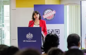 UK Minister for the Indo-Pacific Seema Malhotra speaking at a podium with the UK Government logo, standing in front of a banner featuring a Visa seal and QR code during a campaign launch in Tamil Nadu.
