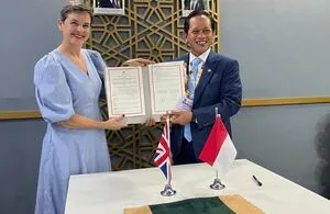 UK Nature Minister Mary Creagh and an Indonesian official hold an open agreement folder while standing behind a desk displaying United Kingdom and Indonesian flags during the COP30 conference.