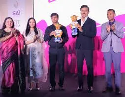 Union Minister Dr. Mansukh Mandaviya and Rajasthan Sports Minister Col. Rajyavardhan Singh Rathore hold mascots on stage with dignitaries during the Khelo India University Games 2025 curtain raiser event.