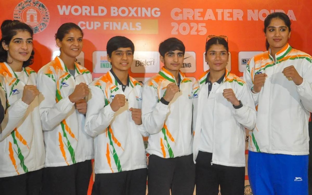 Indian female boxers wearing team tracksuits pose with raised fists against an orange backdrop at the World Boxing Cup Finals 2025 in Greater Noida.