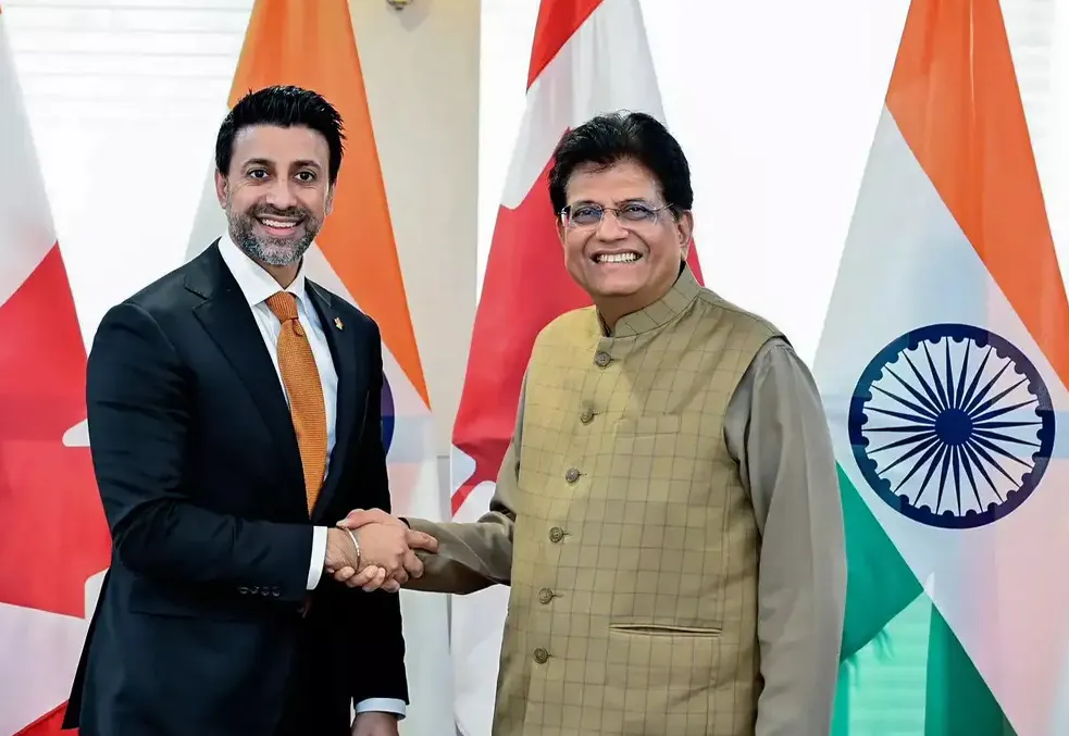 Union Minister Piyush Goyal shaking hands with Canadian Minister Maninder Sidhu in front of Indian and Canadian flags during trade negotiations.