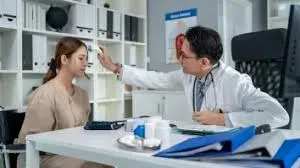 A male doctor in a white coat uses a non-contact digital forehead thermometer to check the temperature of a seated female patient in a medical consulting room.