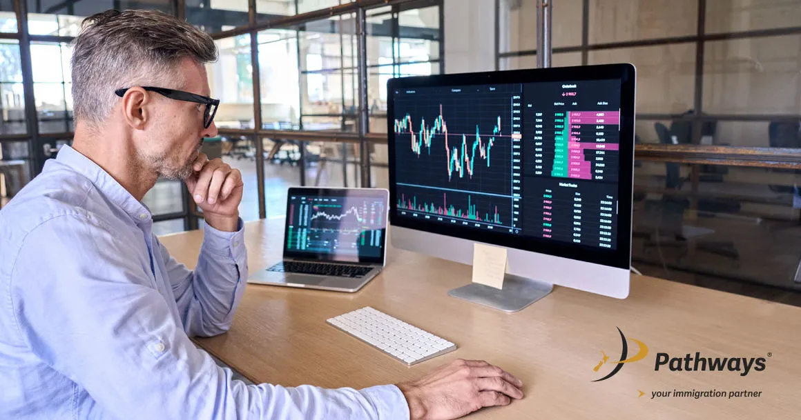 A professional man with glasses analyzing complex financial charts and trading data on a large desktop monitor in a modern office setting