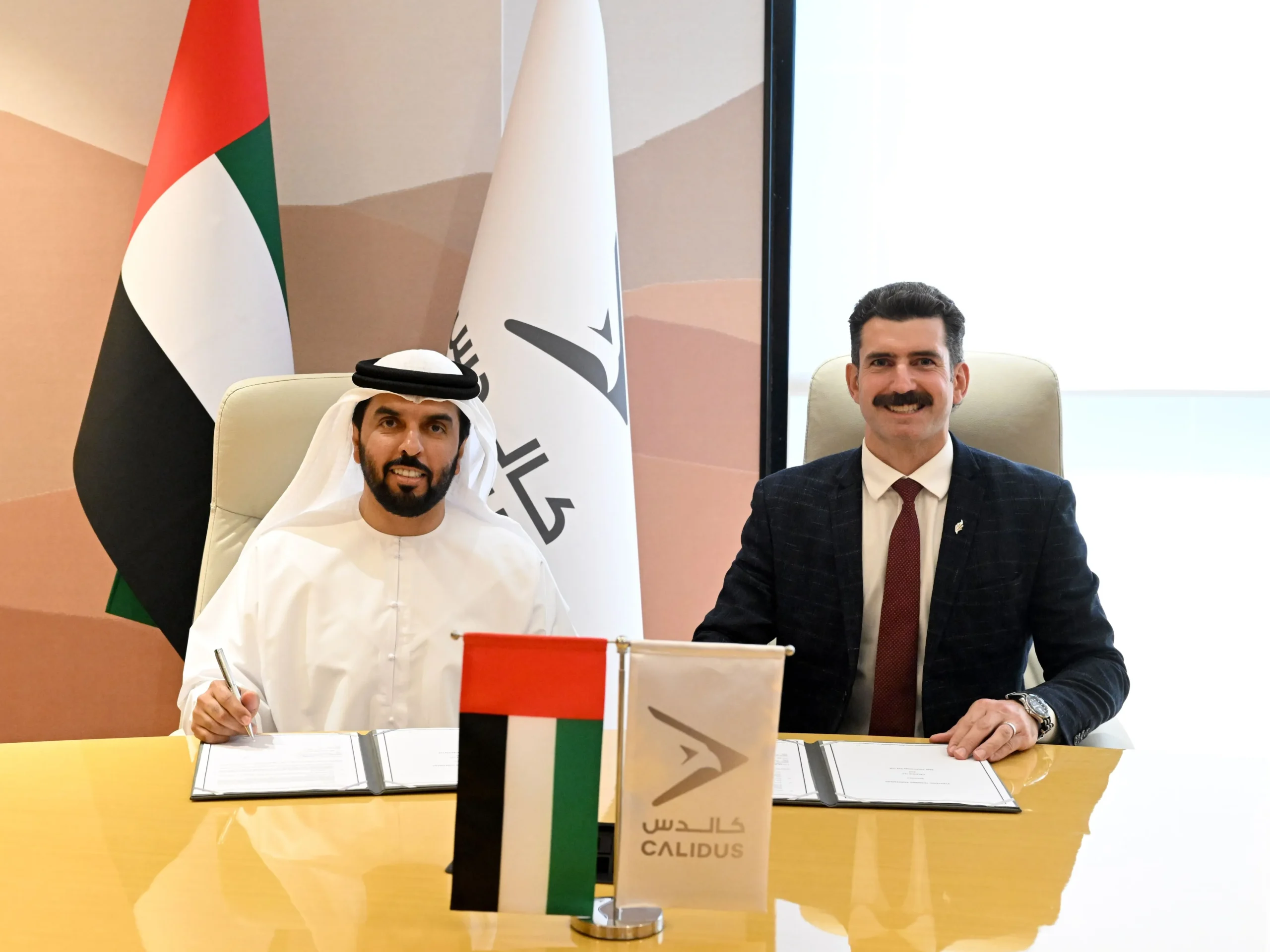 Dr. Khalifa Murad Alblooshi of Calidus Holding Group and Justin Bain of 3ME Technology sitting at a desk signing a teaming agreement with UAE and Calidus flags on the table