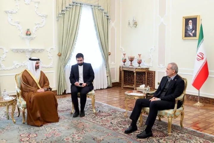 UAE Ambassador Khaled Abdullah Belhoul seated left in traditional dress meeting with Iranian President Masoud Pezeshkian seated right in a suit, with the Iranian flag in the background.