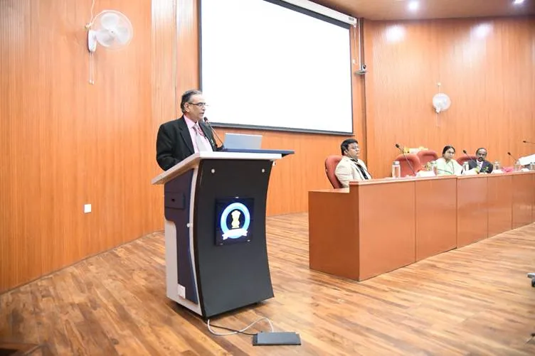 An official stands at a podium with the PCIM&H emblem addressing an audience in a wood-paneled auditorium, while three dignitaries sit at a table on the stage during the inauguration of the ASU&H training program.