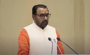 Union Minister of State for Ayush Prataprao Jadhav speaking at a podium, wearing glasses and a cream Nehru jacket over an orange kurta, with microphones in the foreground.