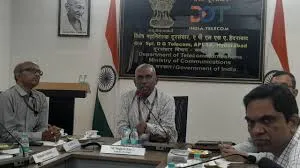 Four Indian government officials, dressed in formal shirts and ties, seated around a wooden conference table during a meeting. The room features the Indian national flag, Ashoka Chakra emblem, a portrait of Mahatma Gandhi, and a prominent banner displaying the Department of Telecommunications (DoT) logo and text in English and Hindi. Microphones, water bottles, and documents are placed on the table.