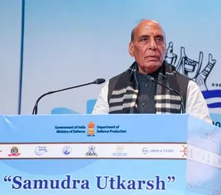 Rajnath Singh, India's Defence Minister, stands at a podium delivering a keynote speech at the Samudra Utkarsh seminar. He wears a traditional white kurta with a black striped vest over it. The backdrop features the blue-and-white logo of the Ministry of Defence, Government of India, Department of Defence Production, and the event title "Samudra Utkarsh" in Hindi and English script.