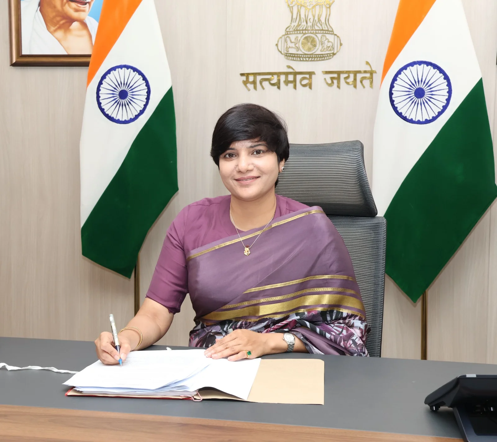 Chief Election Commissioner of India Gyanesh Kumar seated at his desk in the Election Commission of India office, signing documents in front of the national flags and the Ashoka Pillar emblem with the motto "Satyameva Jayate".