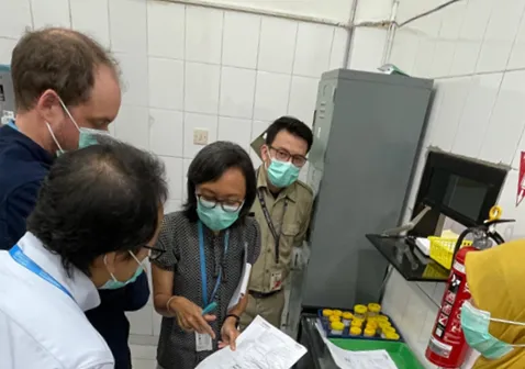 Group of health officials and WHO representatives wearing face masks reviewing documents and discussing TB programme planning in a clinical or laboratory setting during a technical meeting.