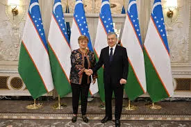 International Monetary Fund Mission Chief Yasser Abdih shakes hands with Uzbekistan's Minister of Economy and Finance Jamshid Kuchkarov in front of Uzbekistan and IMF flags, during the IMF staff visit in Tashkent, Uzbekistan, November 2025. The formal setting features ornate wall decor and gold bases for the flags.