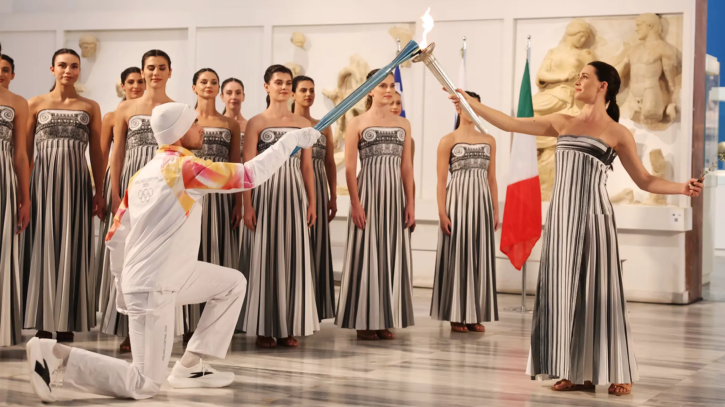 Greek rower Petros Gkaidatzis, first torchbearer of the Milano Cortina 2026 Olympic Torch Relay, receives the Olympic flame from the High Priestess during the handover ceremony at the Archaeological Museum of Olympia, Greece.