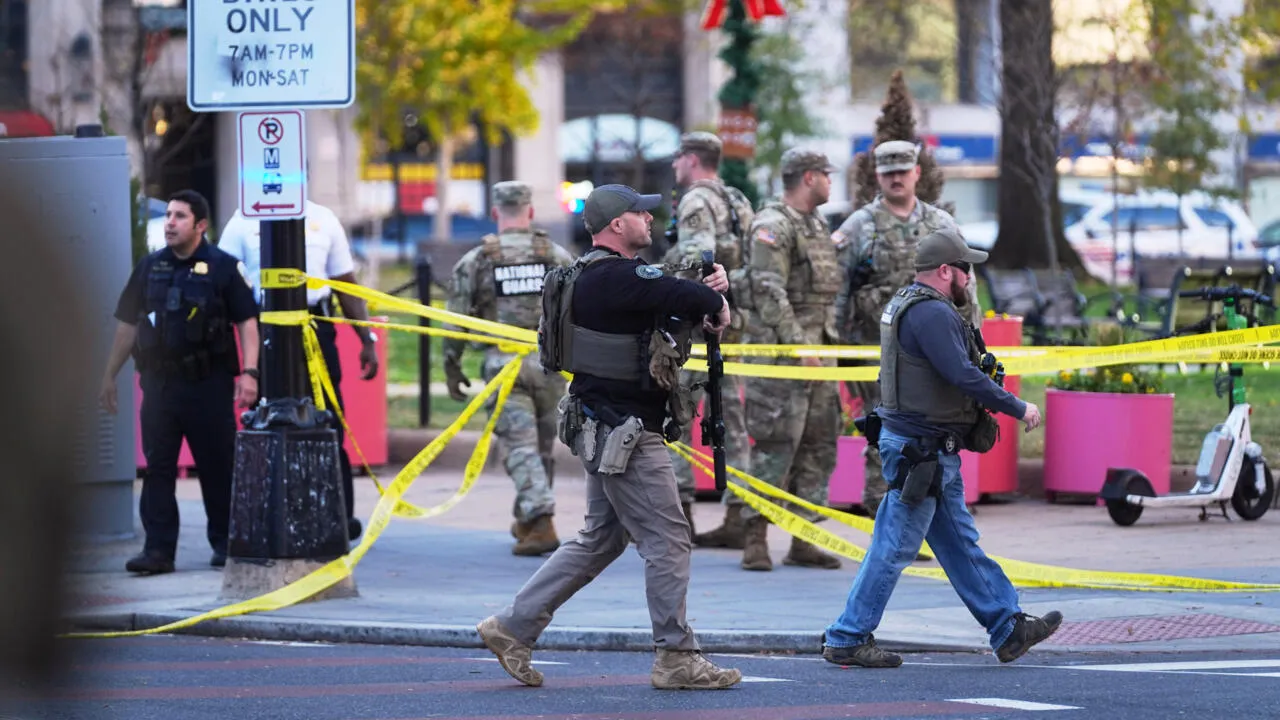 Law enforcement officers and National Guard troops in camouflage uniforms stand behind yellow police tape on a street cordoned off near the White House in Washington, D.C., with holiday decorations including Christmas garlands and trees visible in the background, amid fall foliage and urban elements like traffic signs, trash cans, pink planters, and a scooter.