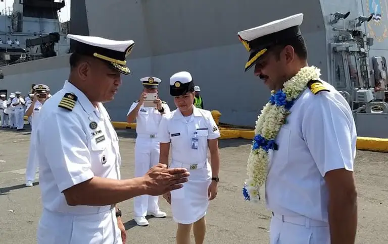 Indian Navy Rear Admiral greeting Philippine Navy officer with traditional garland during the ceremonial welcome of INS Sahyadri at Manila port, Philippines, with crew in white uniforms in formation in the background.