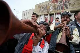 Albanian men in traditional attire play large wooden folk wind instruments during Independence Day celebrations in Tirana, Albania.