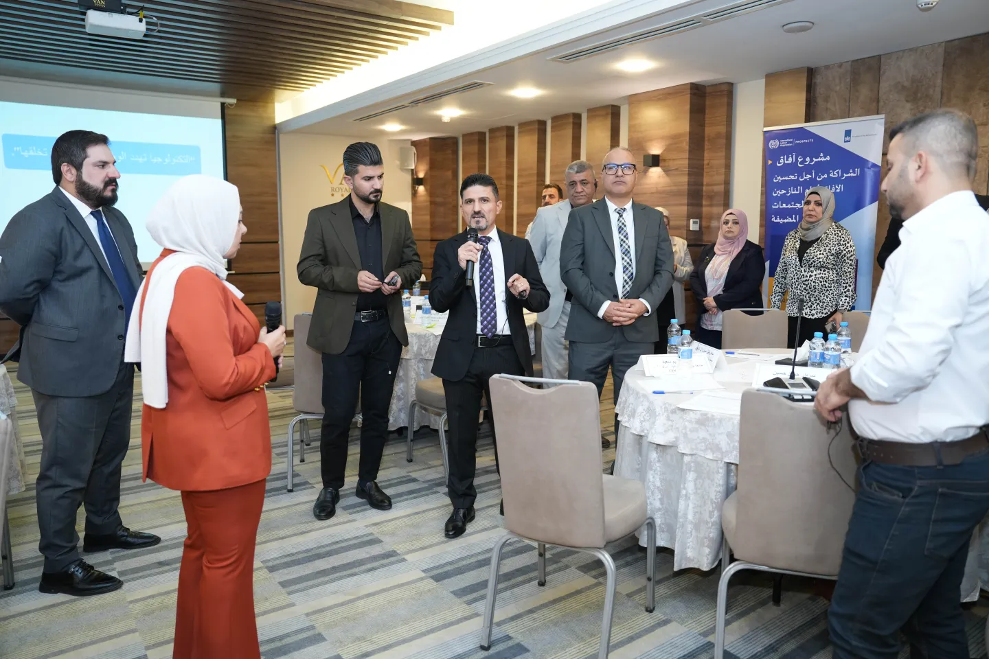 Participants including a woman in red suit and white hijab speaking into a microphone during an interactive session at the ILO advanced training workshop for Public Employment Services and Career Development Centres in Sulaymaniyah, Kurdistan Region of Iraq.